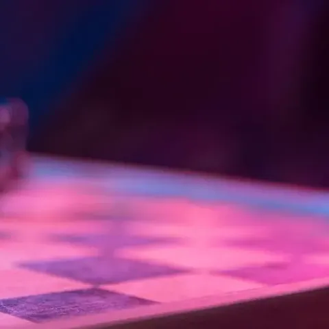 A close-up of a chessboard with dark pieces, highlighted by vibrant blue and pink lighting, creating